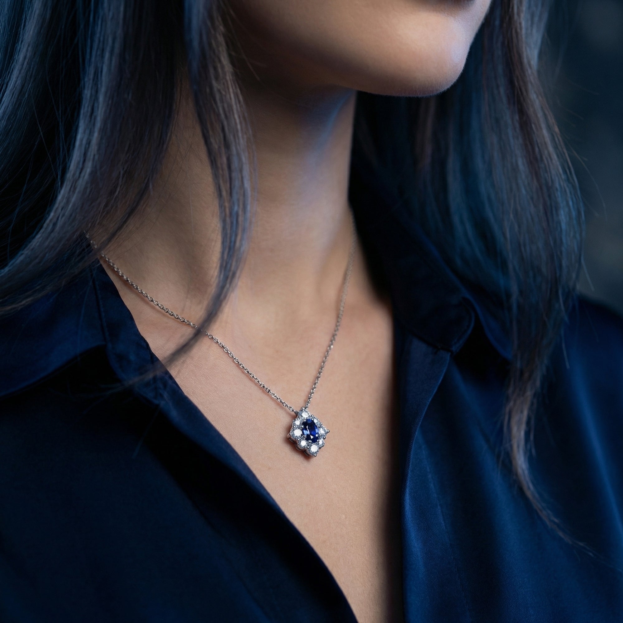 Profile view of a woman wearing the oval tanzanite halo pendant in white gold with a navy silk shirt.