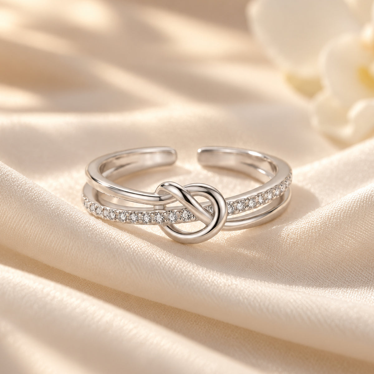Close-up of the silver S925 heart knot ring and clear stone row on cream fabric