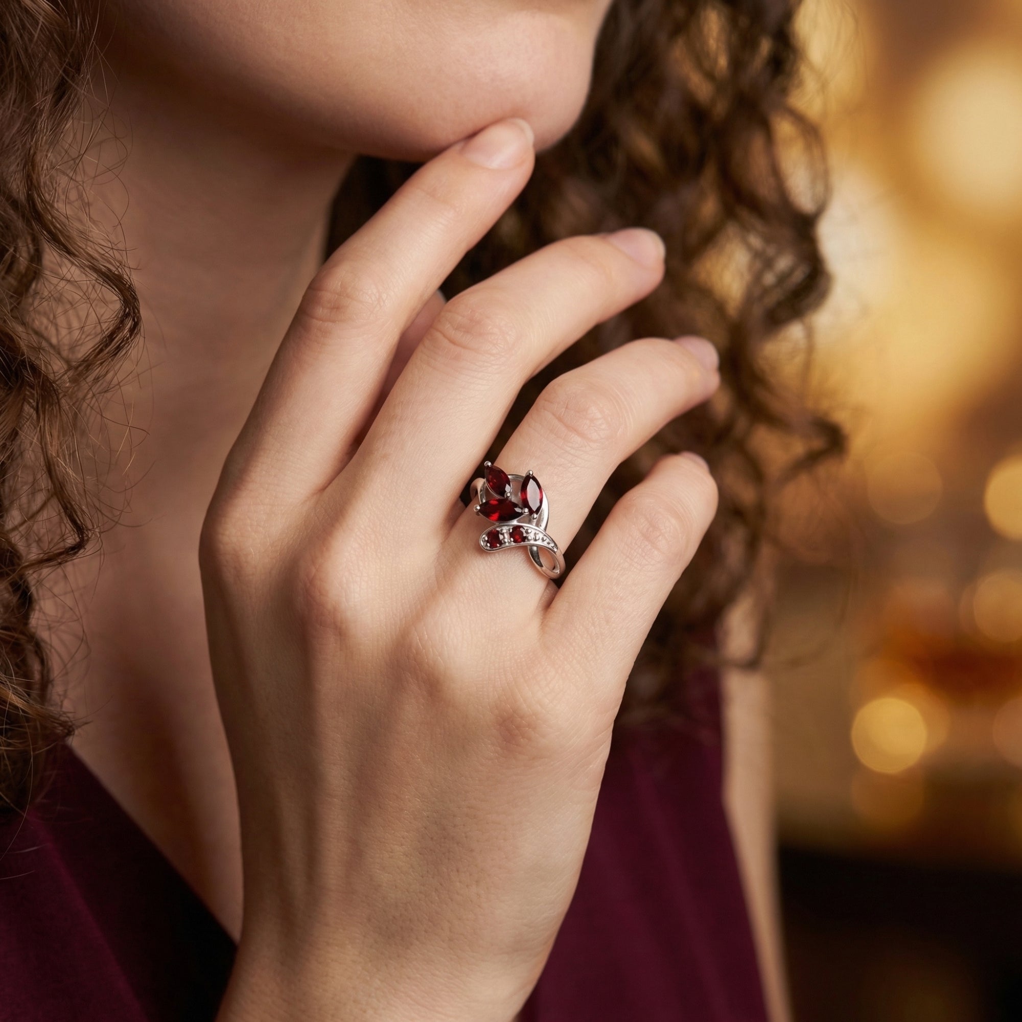 The Elestria sterling silver cluster ring with red garnets worn on a woman's hand, showing its botanical-inspired profile.