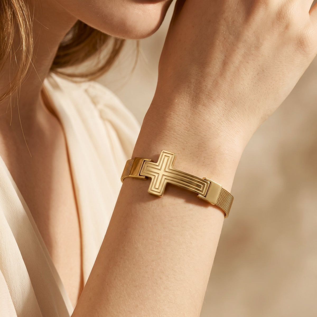 Gold-tone cross mesh bracelet featured on a woman's wrist, wearing a light blouse.