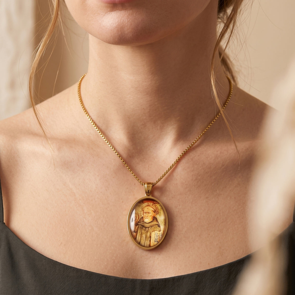 Close-up of a woman wearing the gold-tone oval saint icon pendant necklace with a dark scoop-neck top.