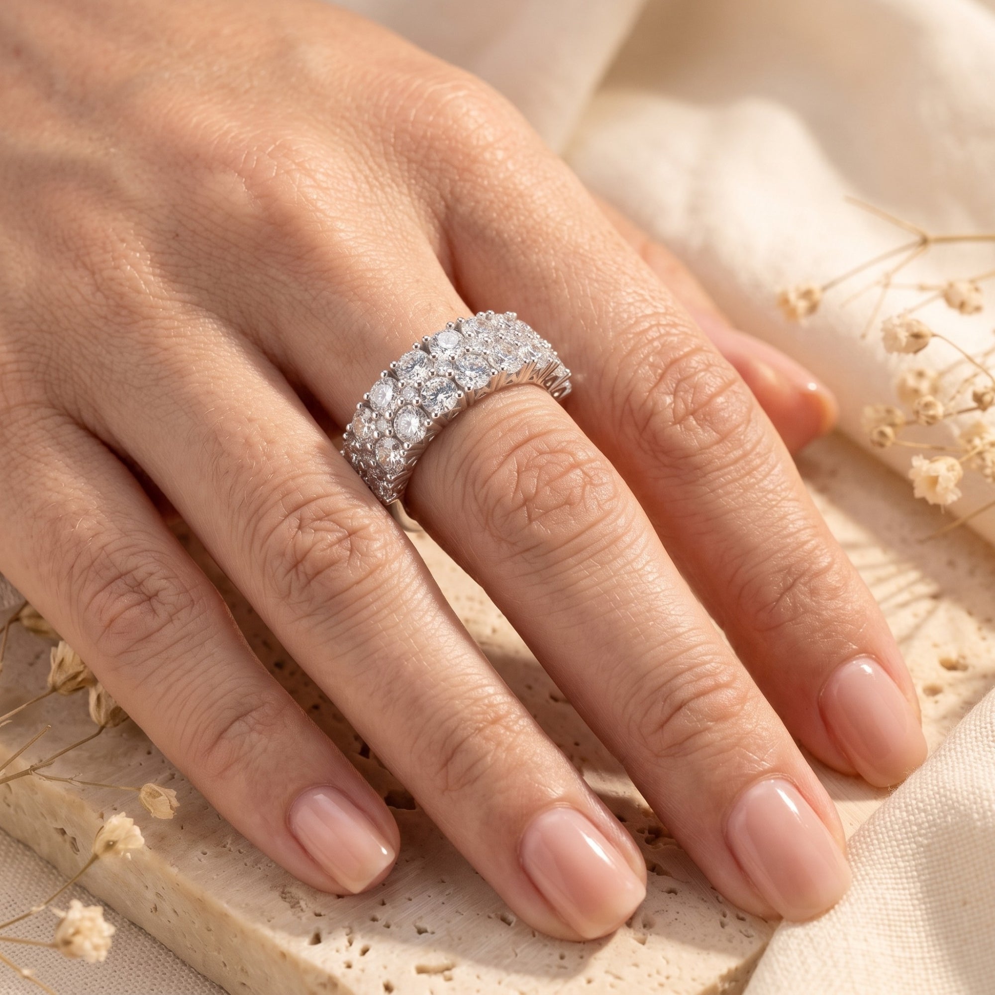 Sterling silver triple row band with round cubic zirconia stones shown on a woman's hand.