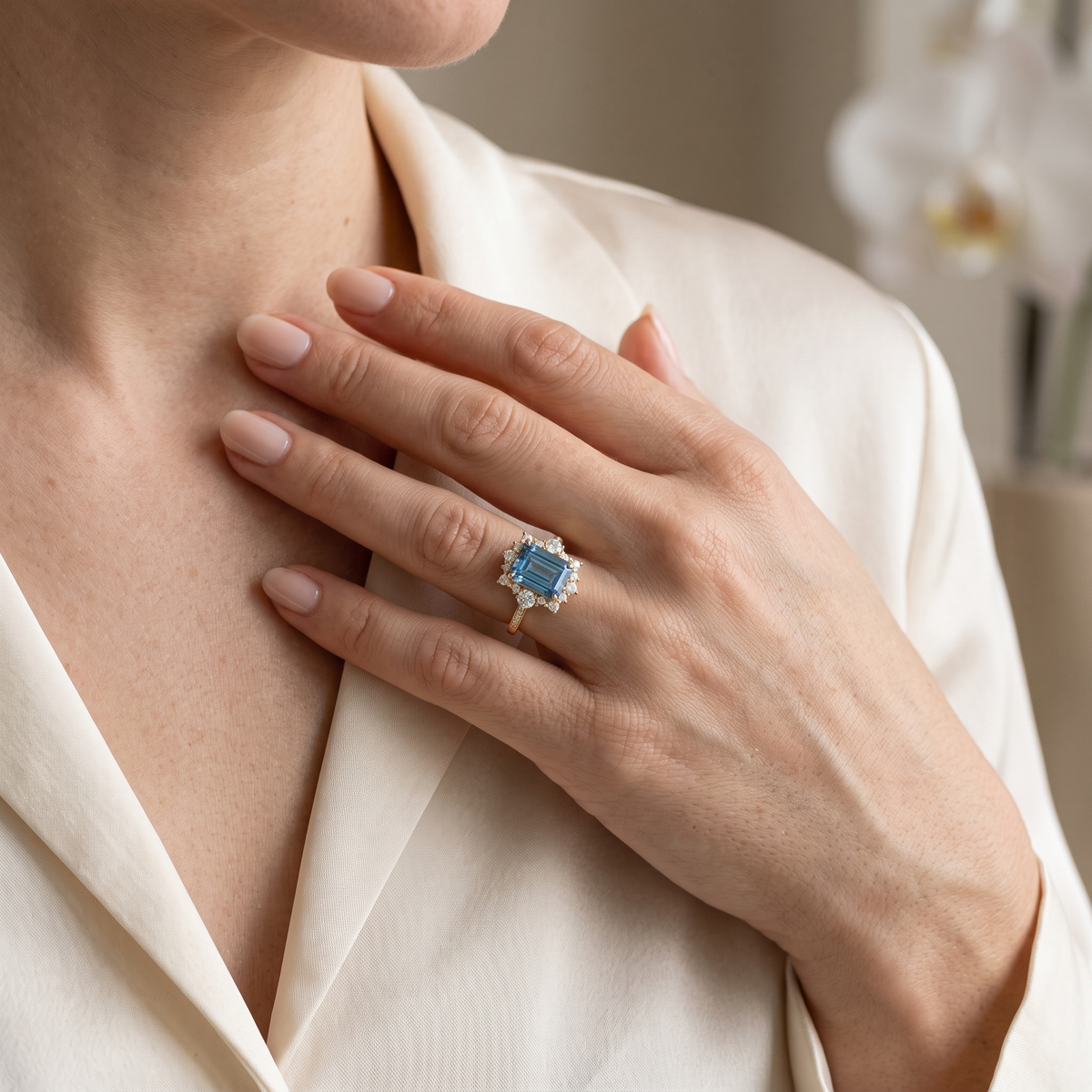 Close-up of a model wearing a yellow gold emerald-cut blue moissanite ring against a silk outfit.