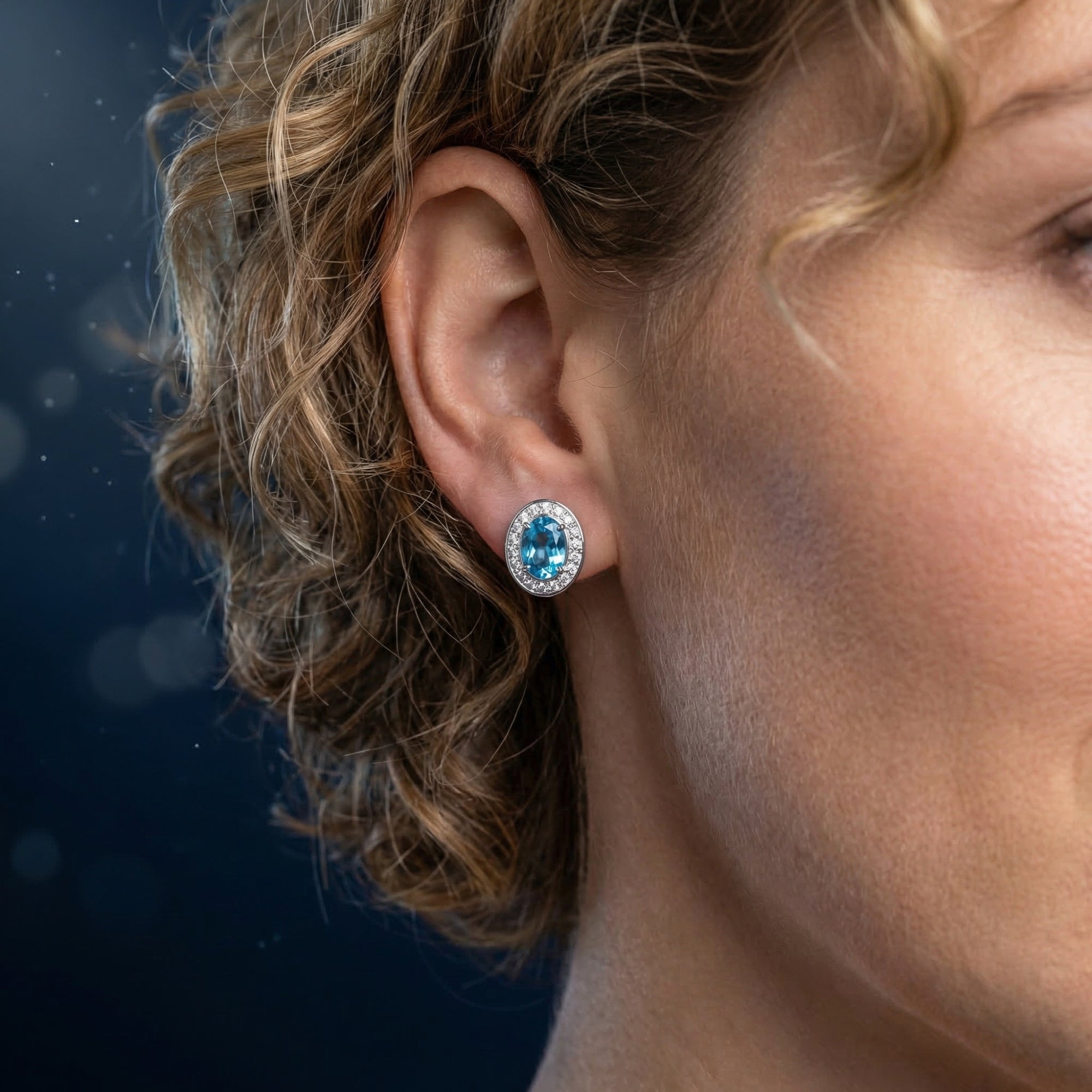 Side profile of a woman wearing an oval natural blue topaz halo stud earring in white gold.