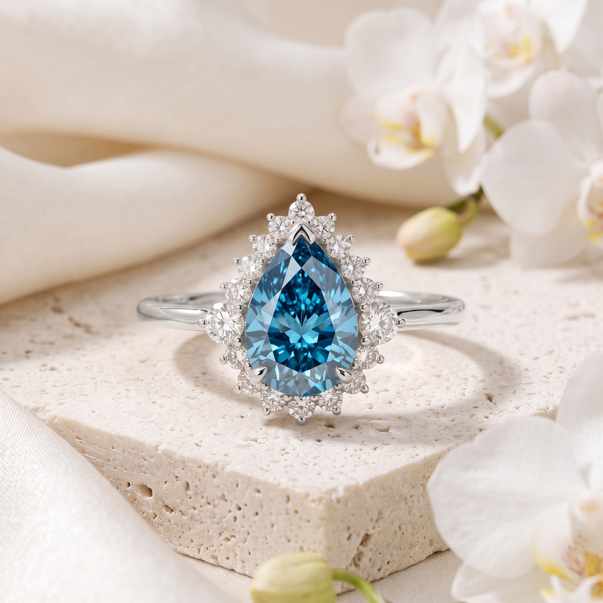 Pear-cut blue moissanite halo engagement ring in white gold displayed on a textured stone.