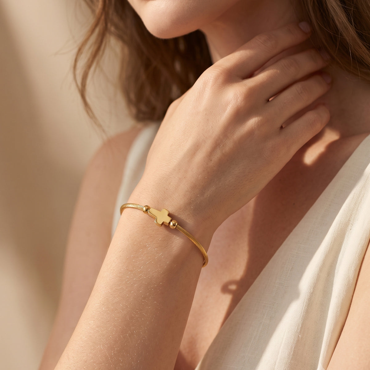 Close-up of a model wearing the gold-tone cross cable bracelet on her wrist, with her hand near her neck.