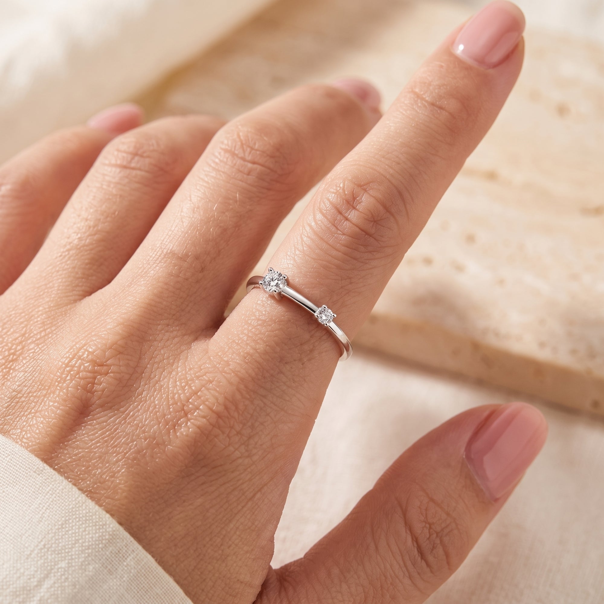 Silver asymmetric bypass ring with two simulated diamonds shown on a finger for scale.