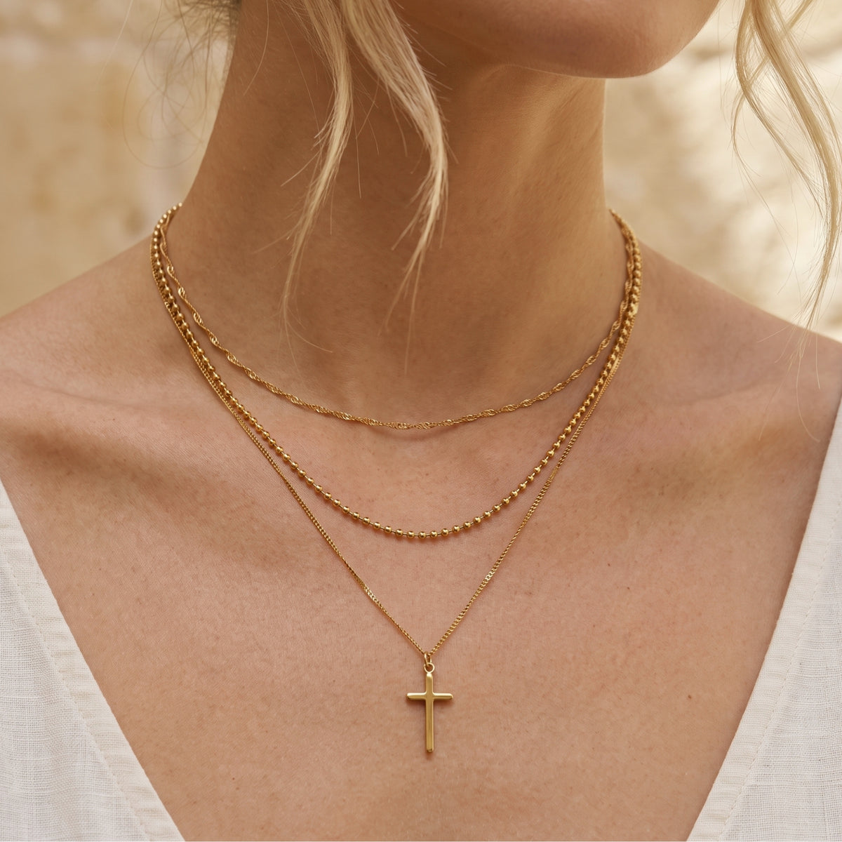 Front view of a woman wearing a gold-tone three-strand layered cross necklace on her chest.
