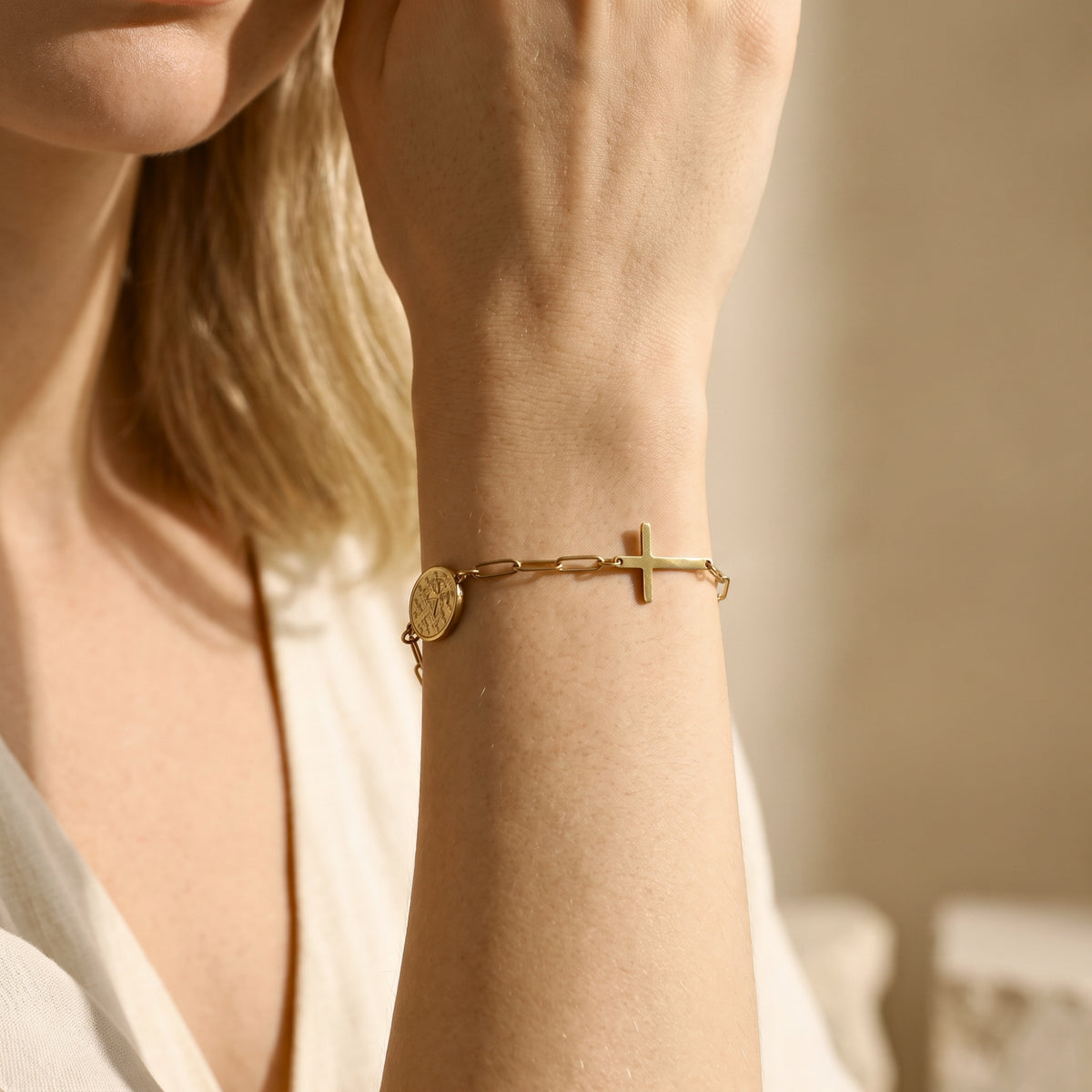 Close view of a wrist wearing the gold-tone link bracelet, with the cross charm extending across the wrist.