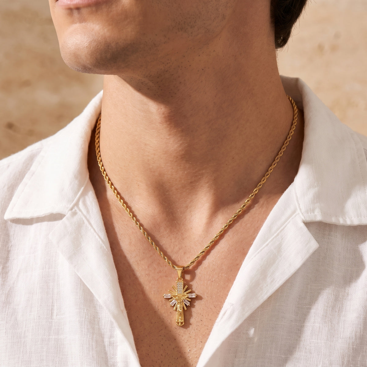 Front view of a man wearing the gold-toned sunburst cross necklace over an open white linen shirt.