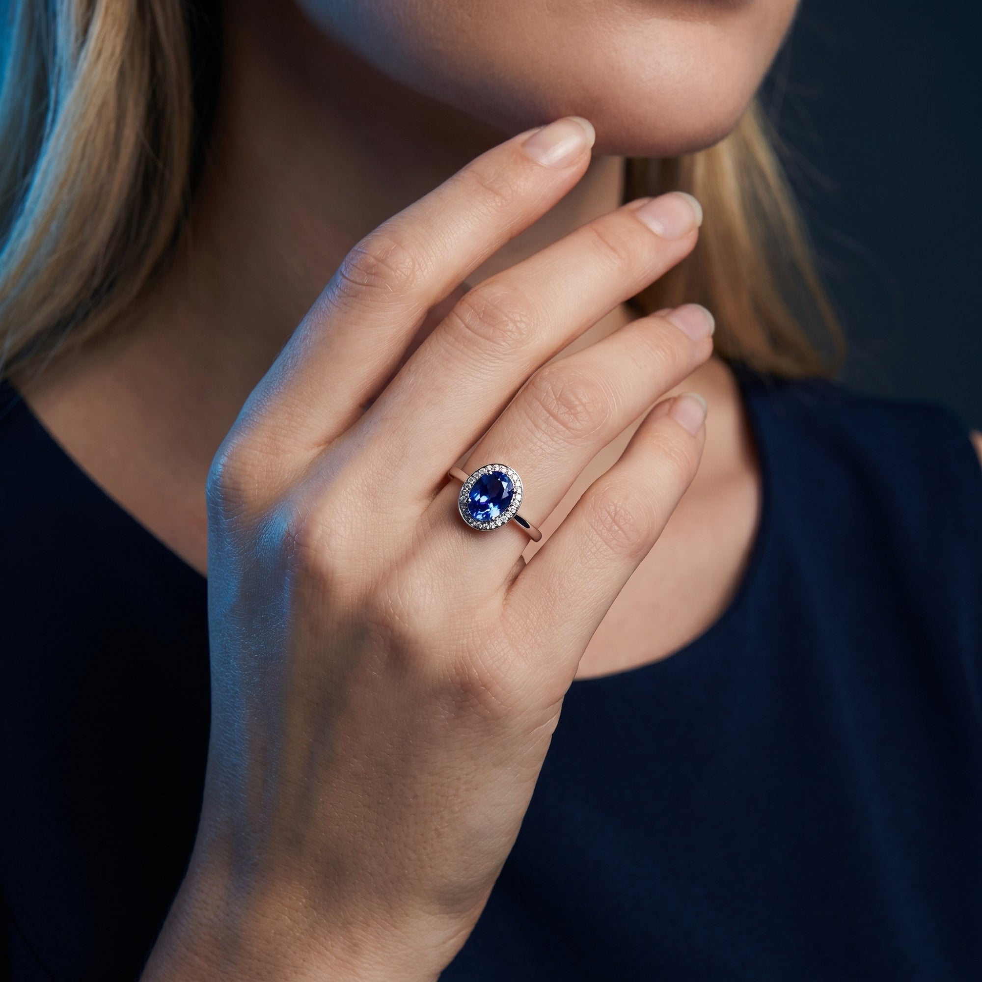 Woman wearing the Lirael oval tanzanite halo ring in 18K white gold, showing scale on the finger.