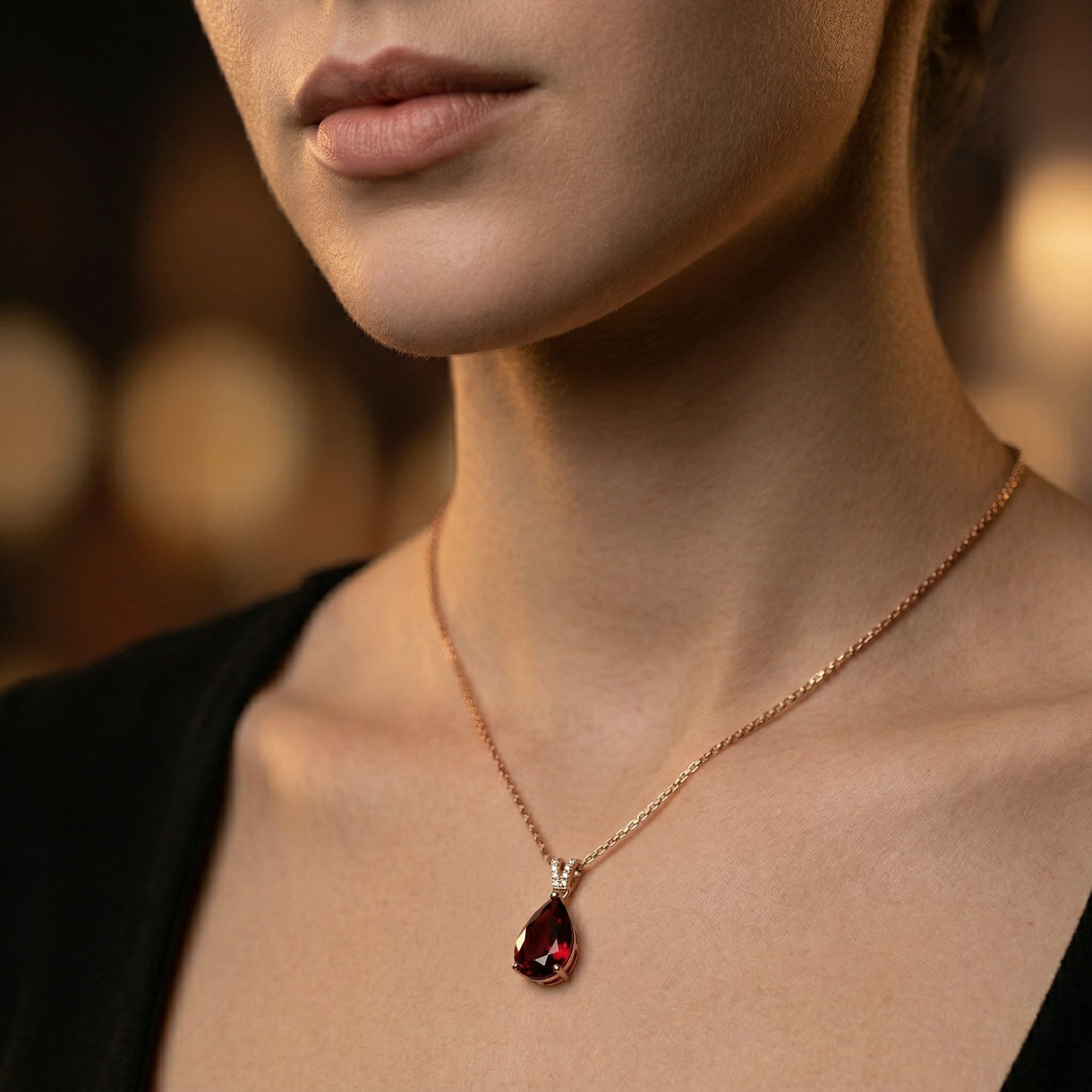 18K rose gold necklace with a pear cut garnet pendant worn by a model against a dark background.