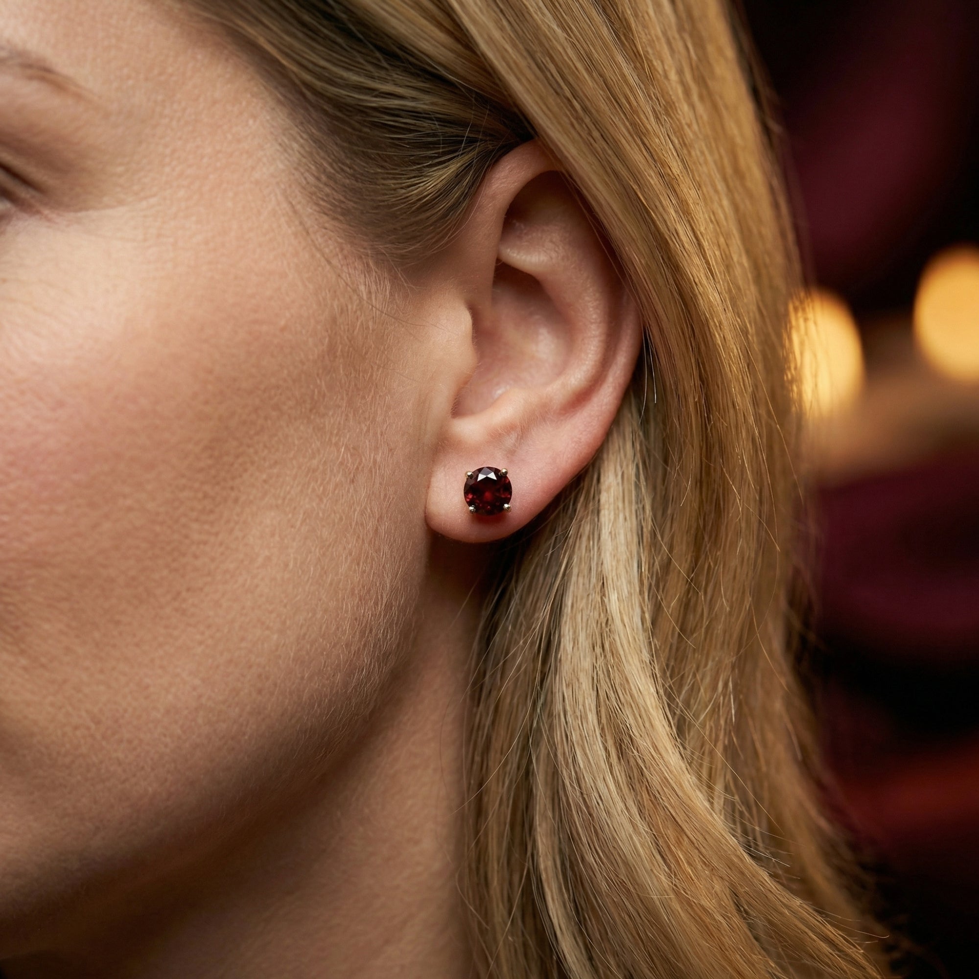 Profile view of a woman wearing a large round-cut red garnet stud earring set in 18K white gold.