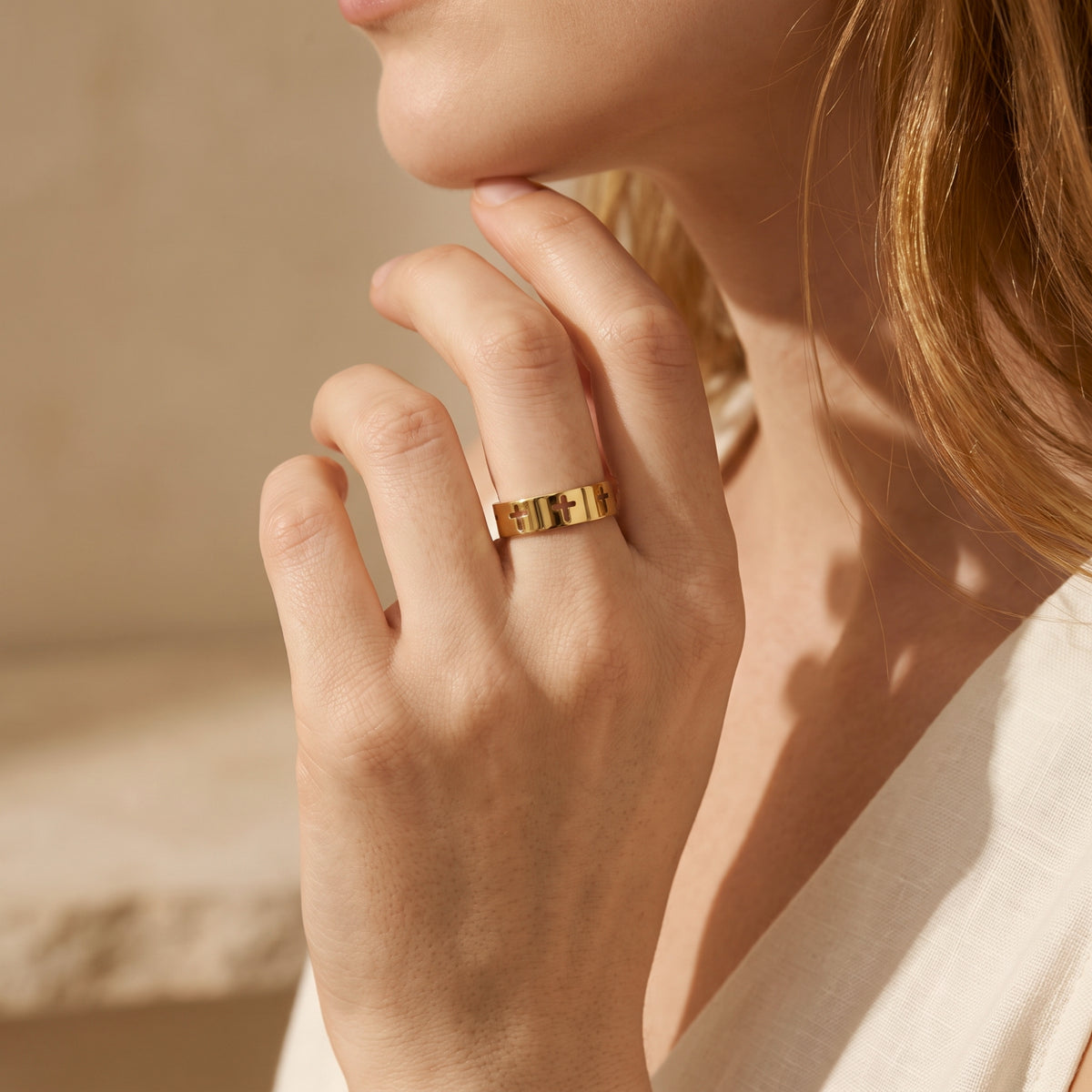 Side view of a model wearing the gold-tone cutout cross band ring while touching her chin.