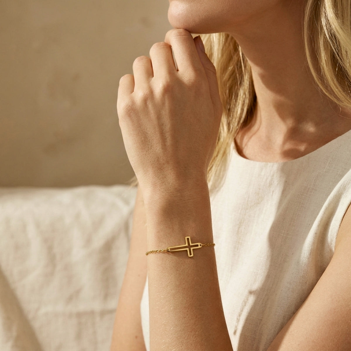 Close portrait of a model resting her hand near her chin while wearing the gold cutout cross bracelet.