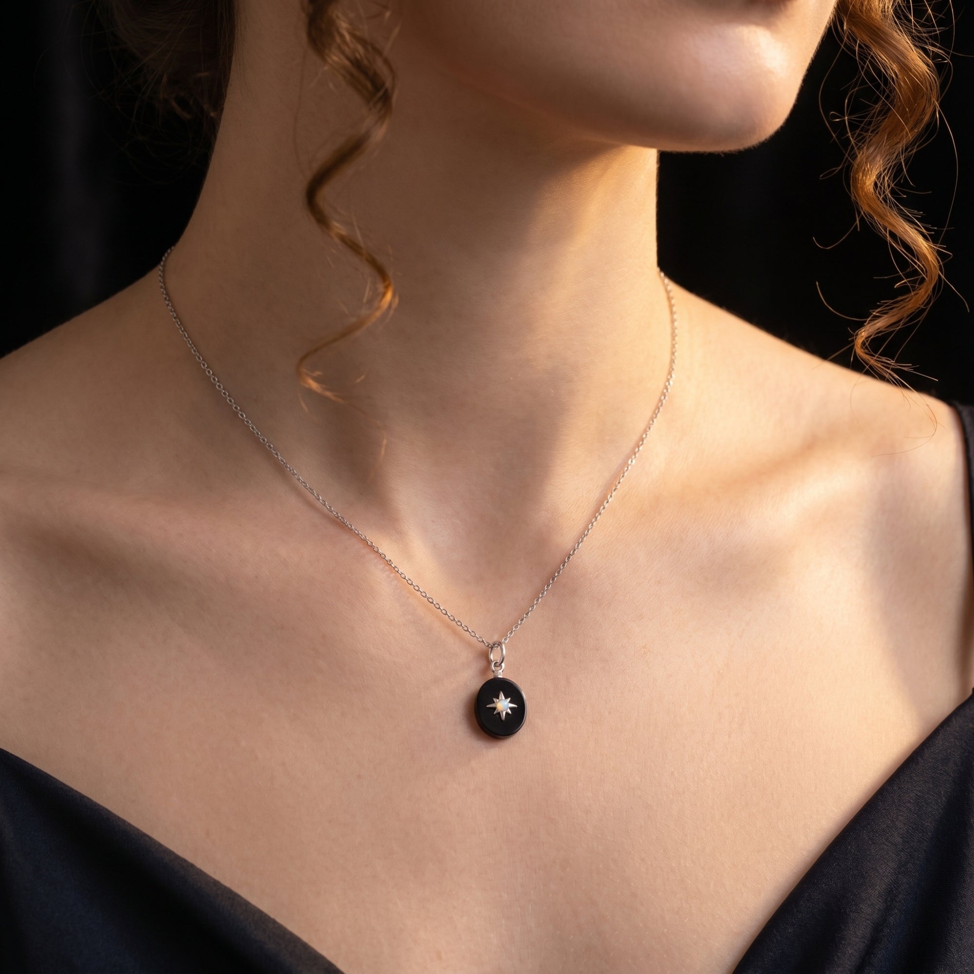 Silver oval black onyx necklace with a starburst detail worn by a model against a dark background.