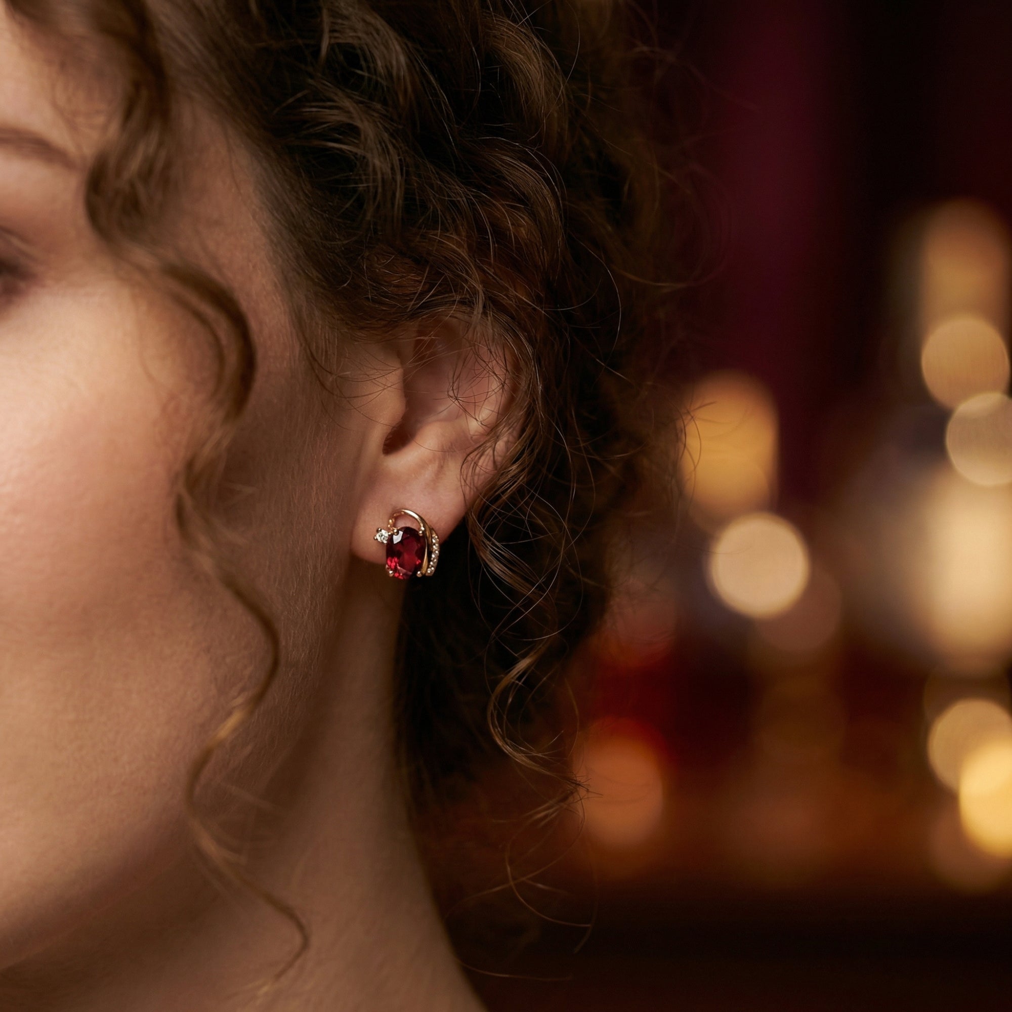 Close-up of a model wearing the Carisia 18K rose gold drop earring with a vibrant oval cut garnet.