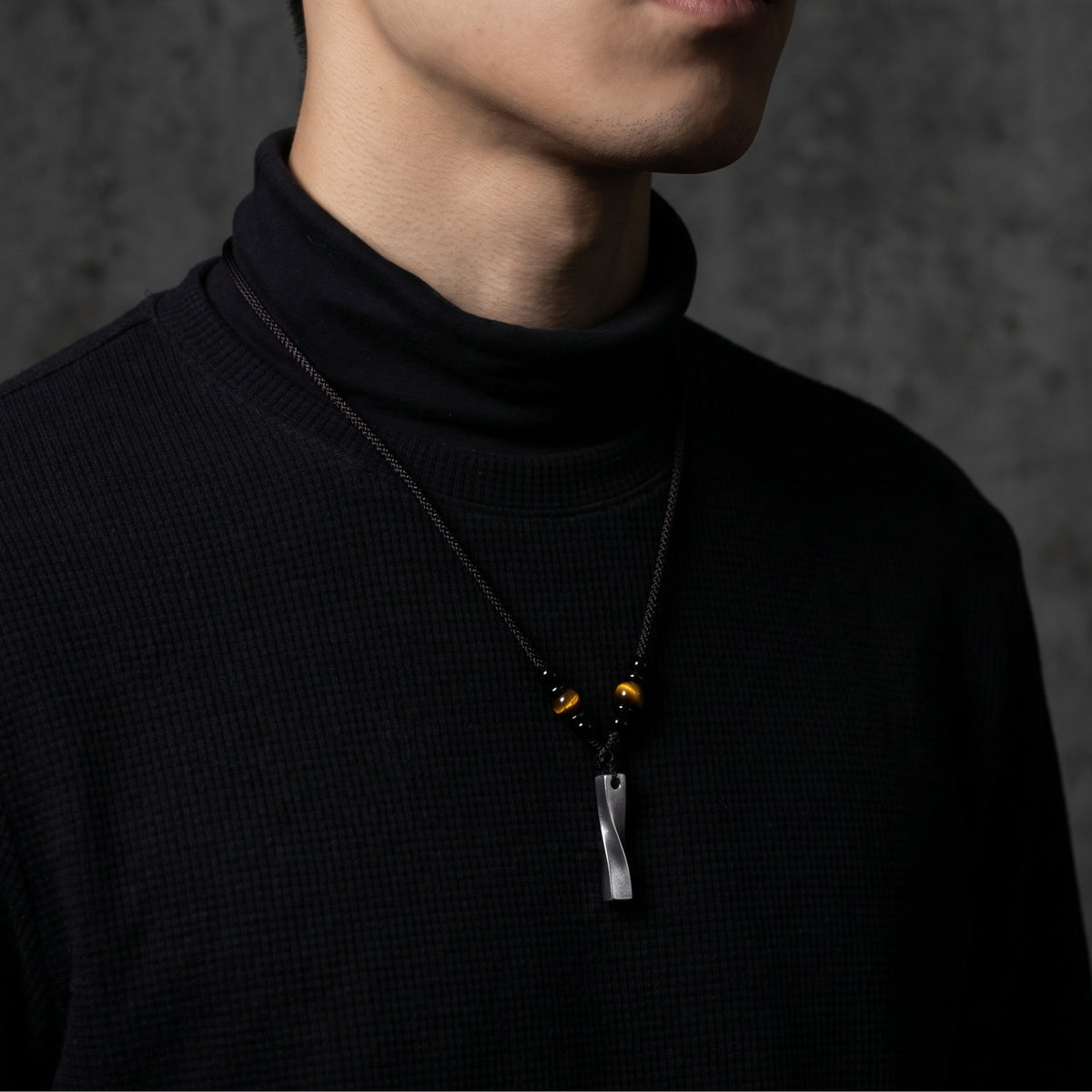 Model wearing the twisted silver bar pendant necklace over a black ribbed turtleneck.