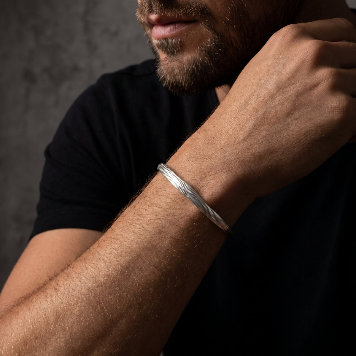 Close-up angled view of a man wearing a bark-textured silver open cuff bracelet on his wrist.