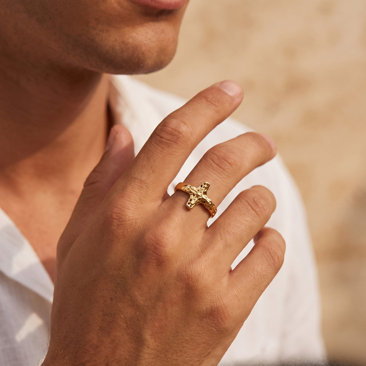 Gold-tone sculpted cross ring worn on a man's hand in a close-up lifestyle view.