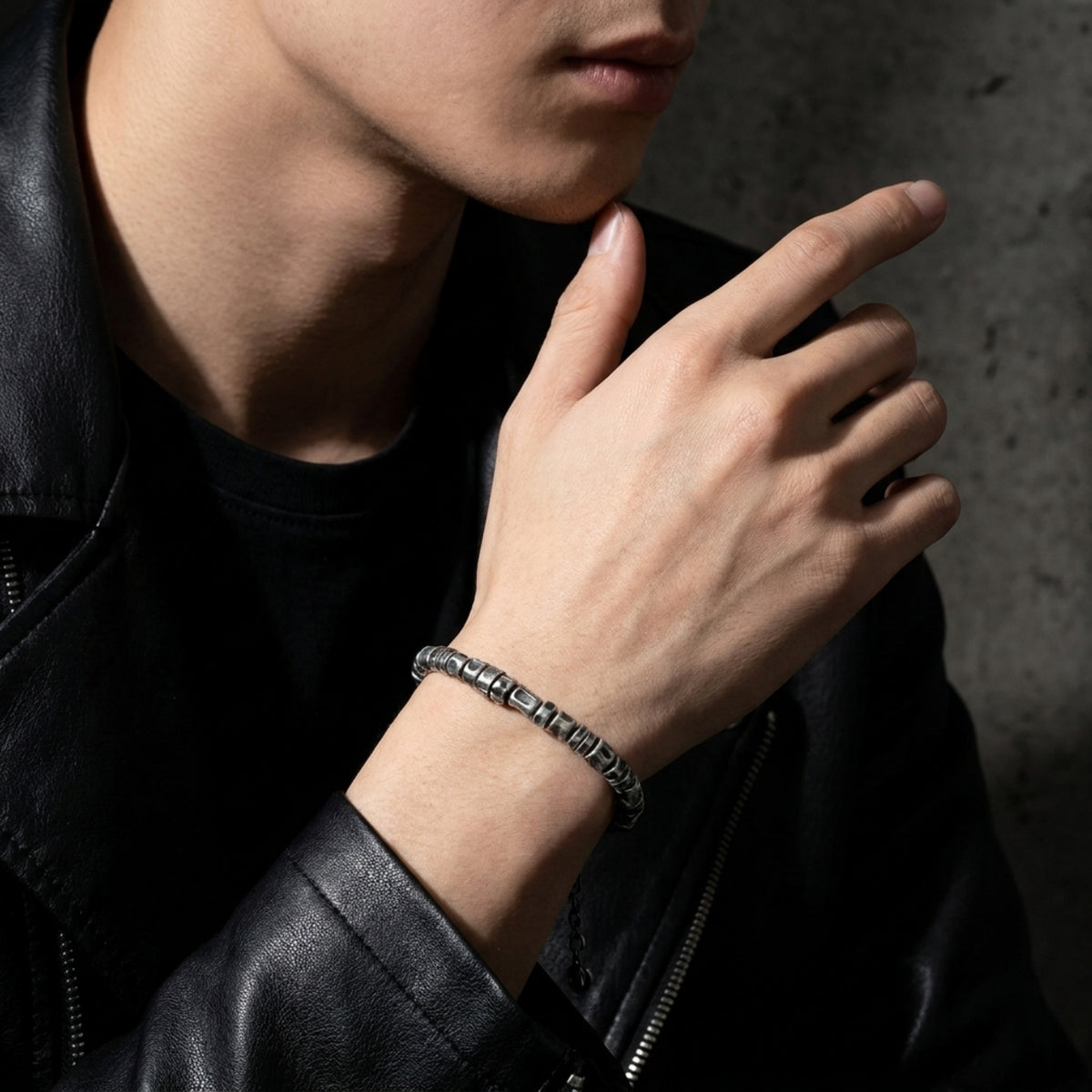 Textured silver barrel-link bracelet worn on a wrist with a black leather jacket and black shirt.