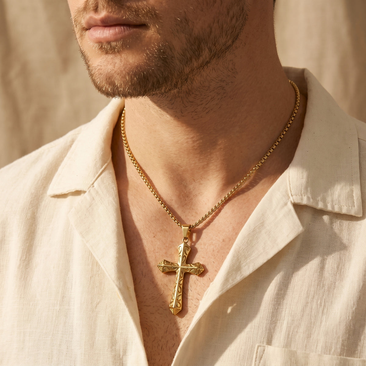 Medium view of a man wearing the gold-tone scrollwork cross necklace with an open cream linen shirt.