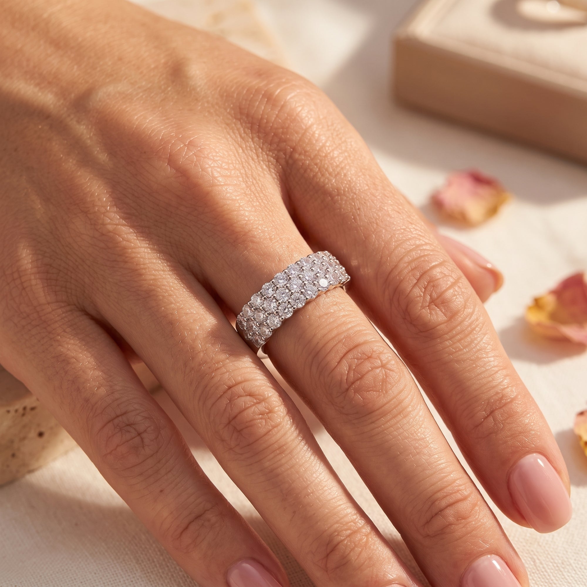 Sterling silver multi-row pavé ring with round stones on a hand with rose petals.