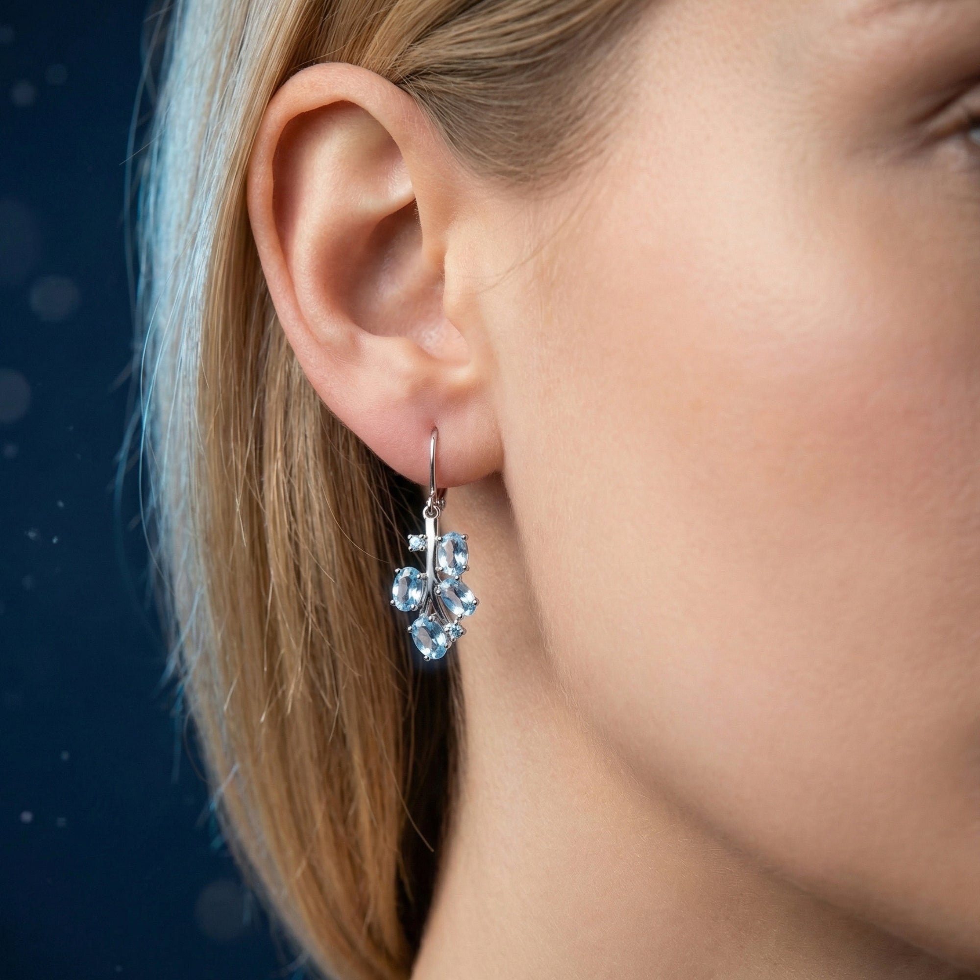 Close-up of a silver Nereia drop earring with natural blue topaz clusters worn on a woman's ear.