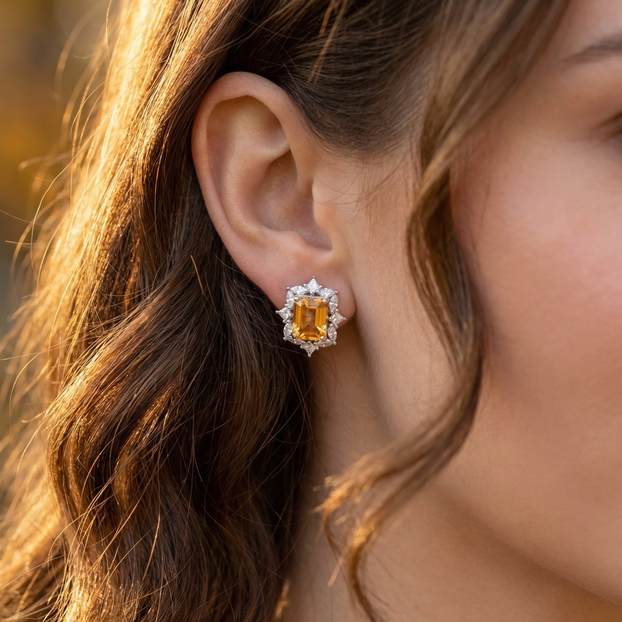 Side profile of a woman wearing a natural citrine emerald cut earring with a sparkling diamond halo.