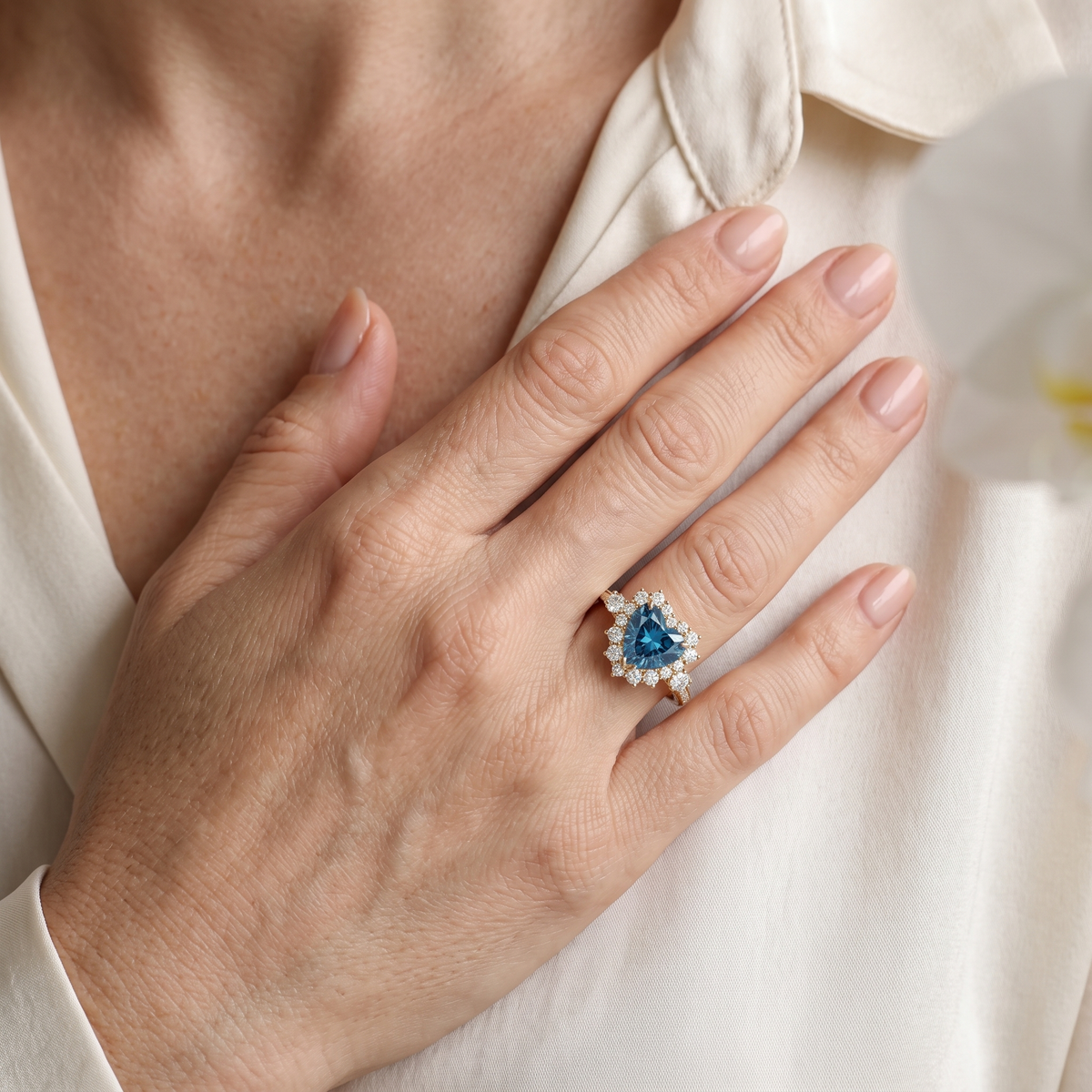 Close-up of a model wearing a heart-shaped blue moissanite halo ring in yellow gold.