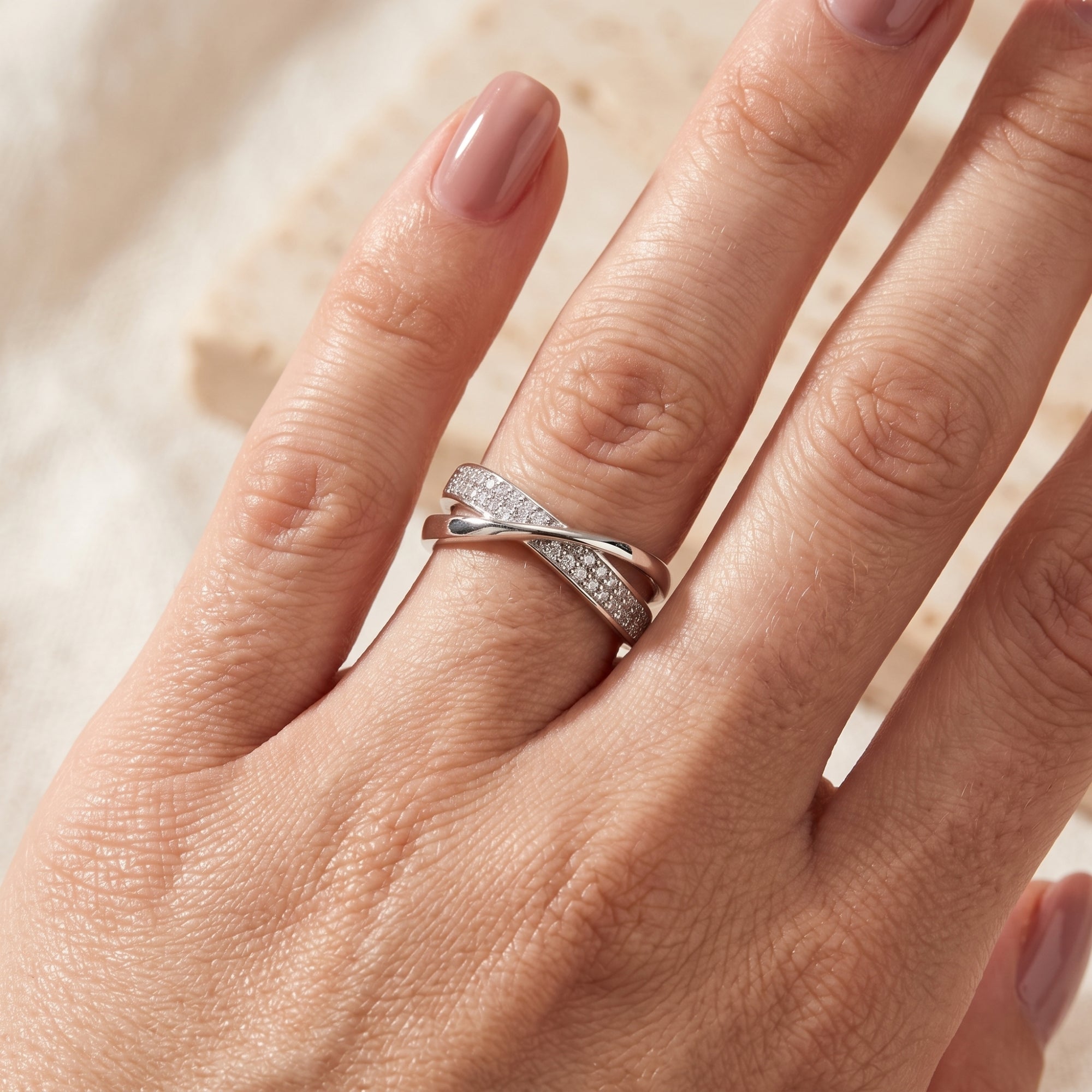 Top-down view of silver crossover ring with pavé stones on a hand.