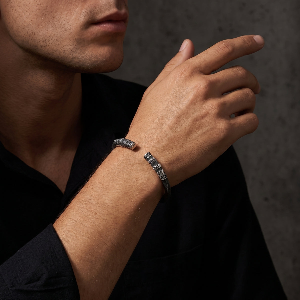 Man wearing the carved silver cuff bracelet on his wrist with his raised hand near his face.