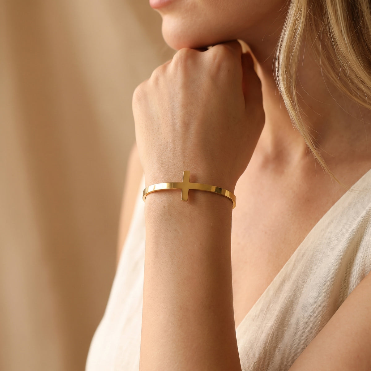 Woman wearing a gold-tone cross cuff bracelet with her hand raised beneath her chin.