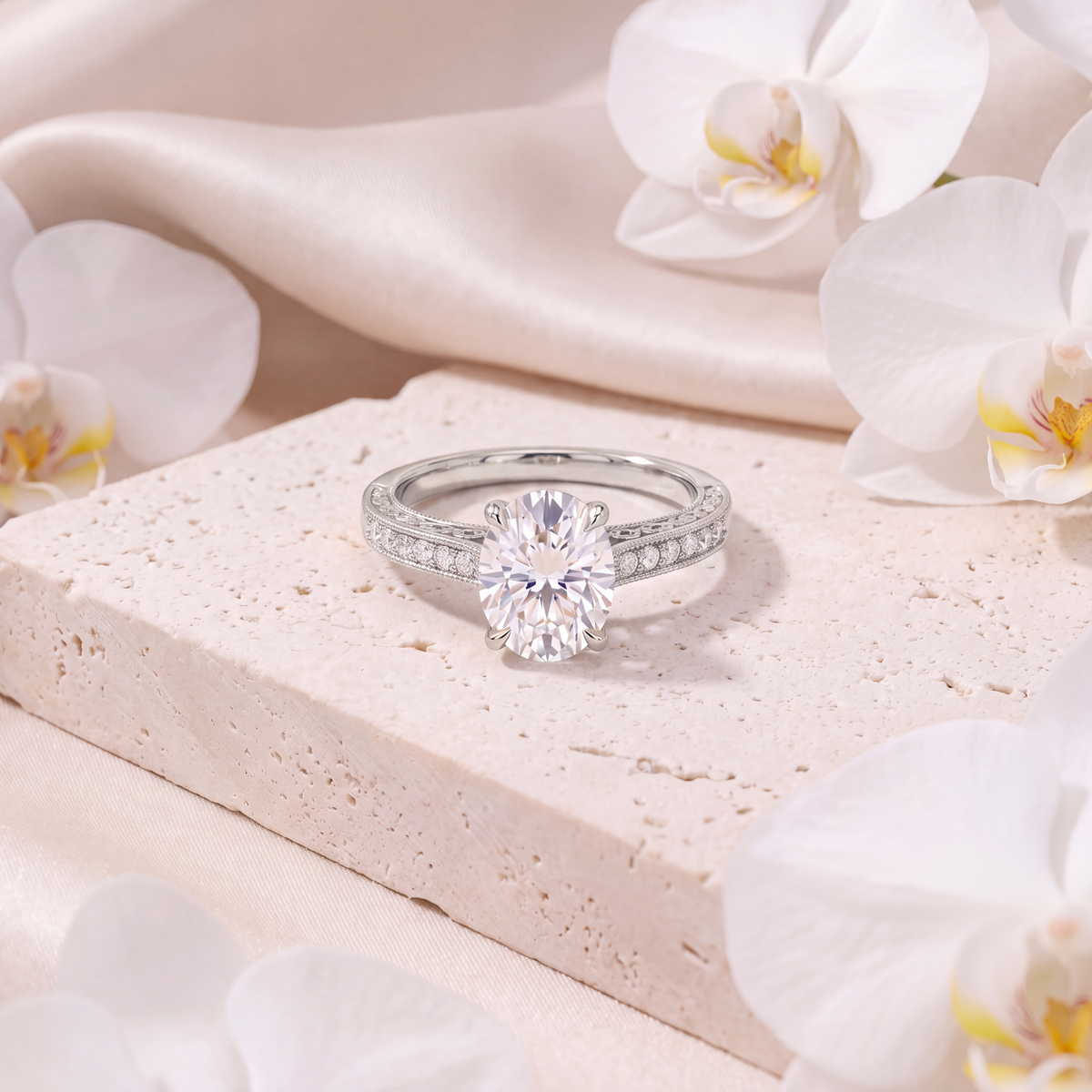 White gold oval moissanite engagement ring with an ornate accent band resting on a stone surface.