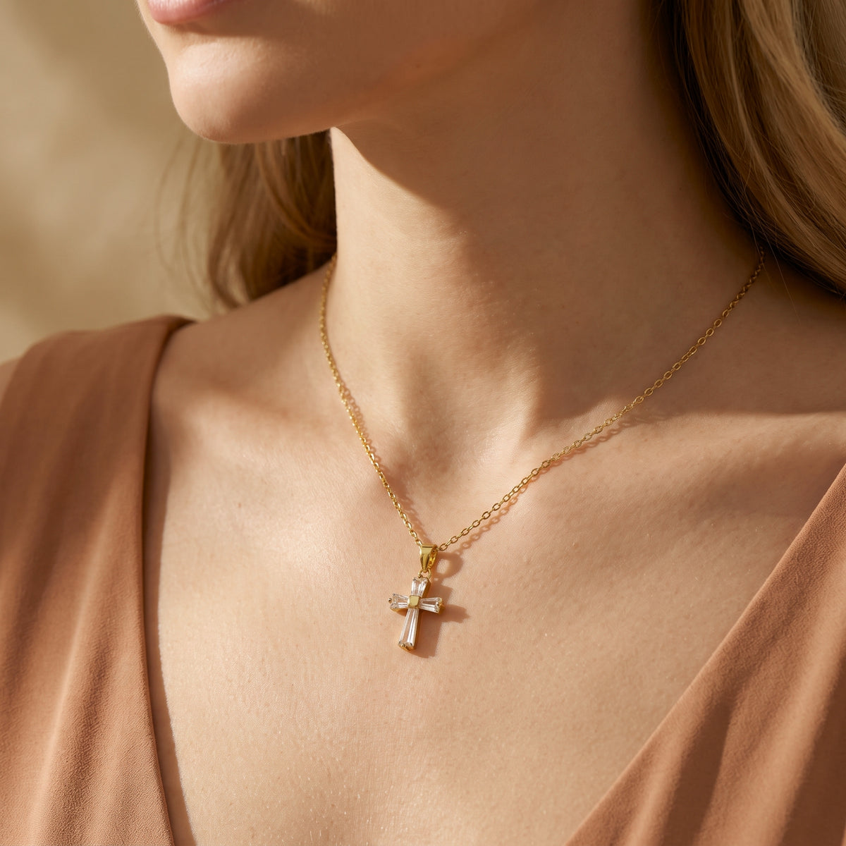 Model wearing the gold baguette cross necklace over a tan dress, with the pendant centered on the neckline.