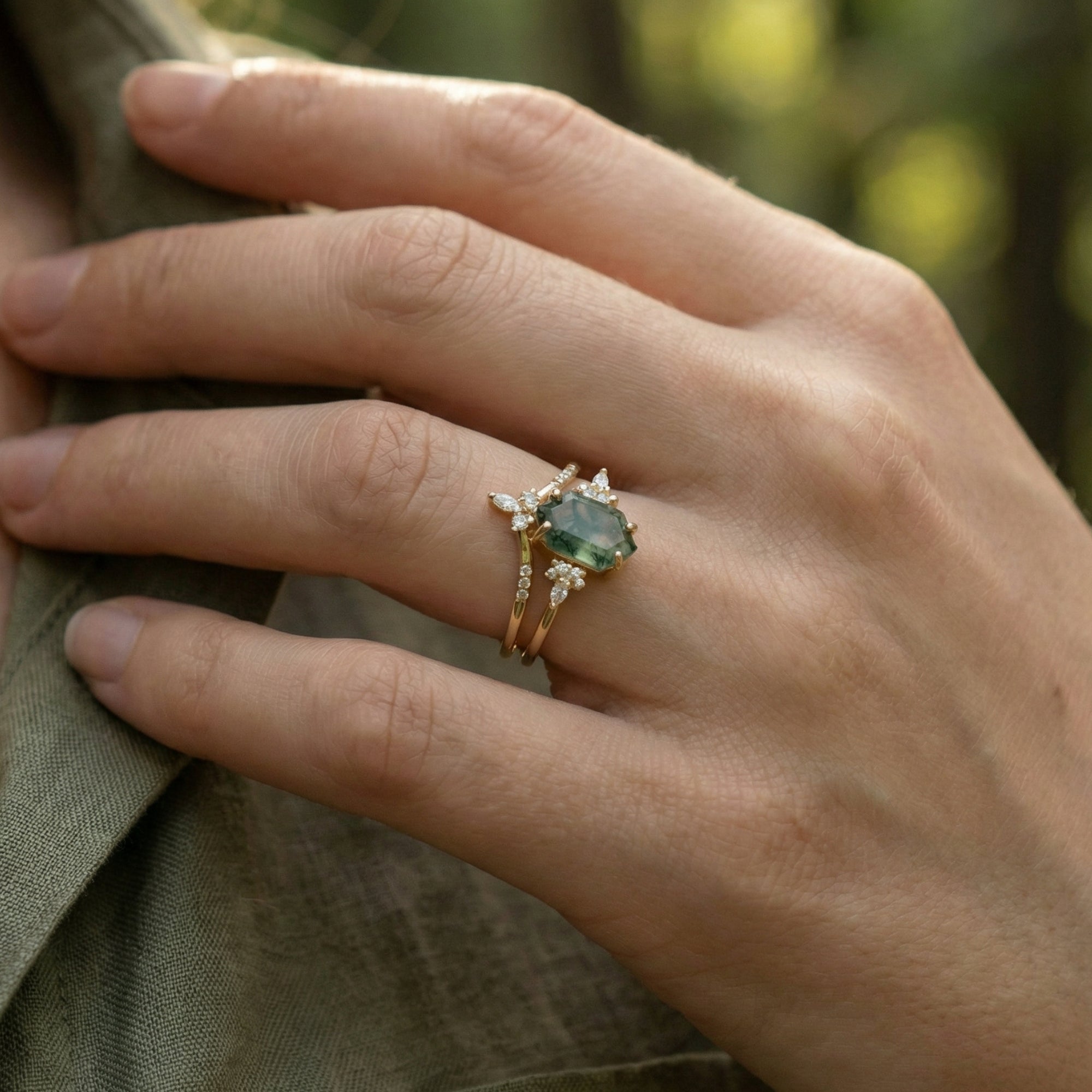 Hexagonal cut moss agate gold ring set worn on a finger to show size and scale.