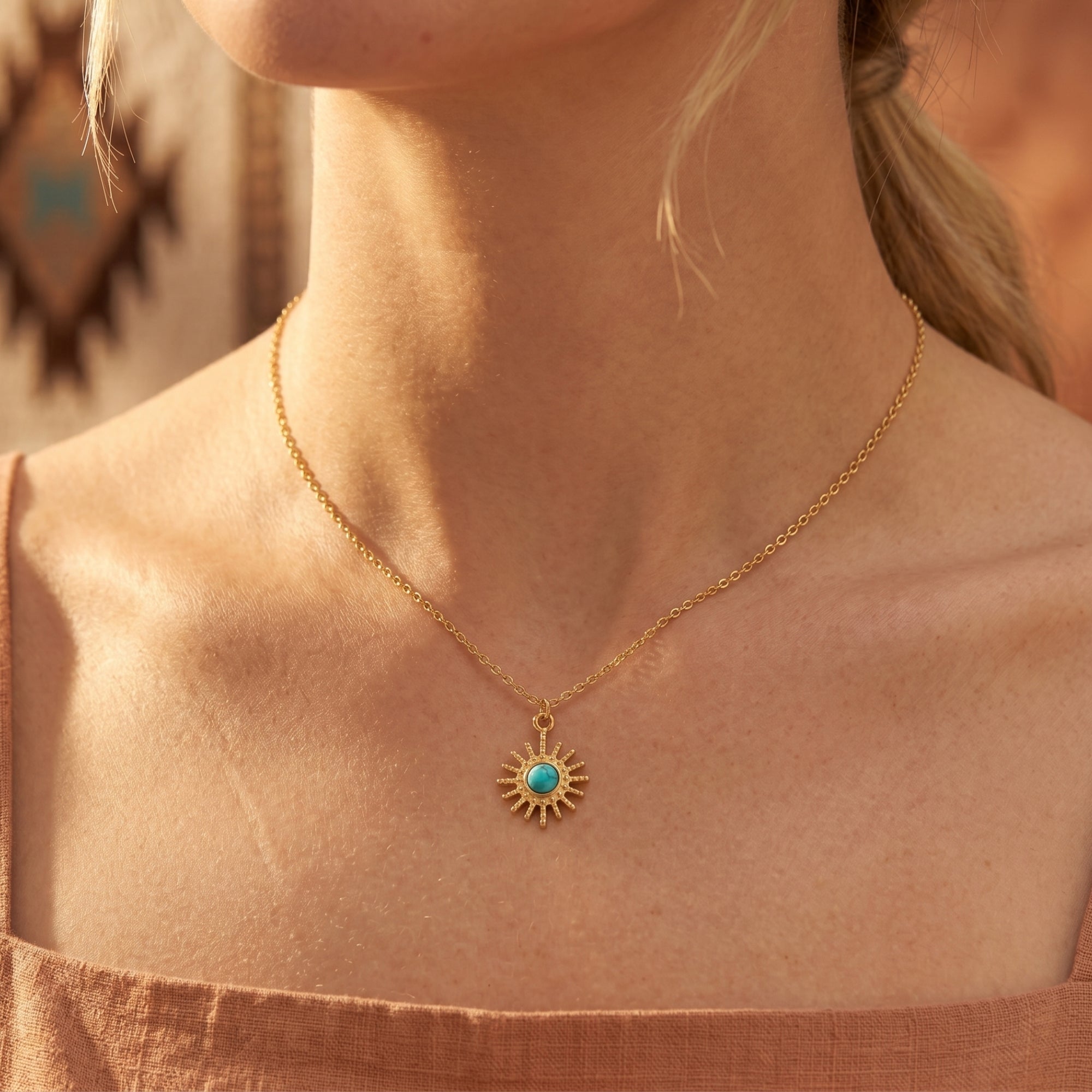 Front view of the 18K gold sunburst necklace with a turquoise cabochon worn by a model in sunlight.