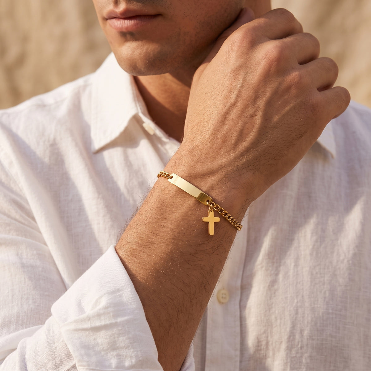 Man wearing the gold-tone cross ID Figaro bracelet on his wrist with a white button-down shirt.