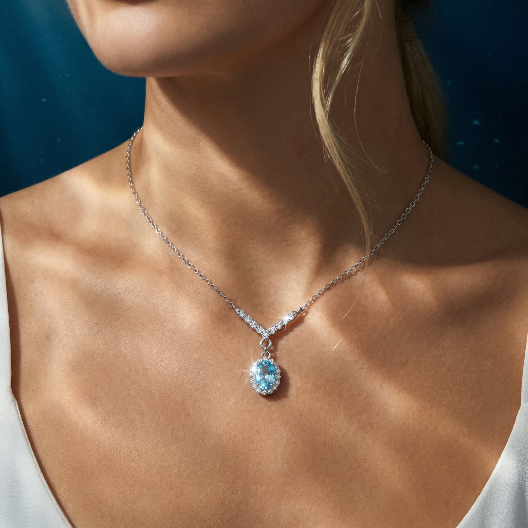 Front view of a model wearing the oval aquamarine halo pendant necklace in sterling silver against a blue background.
