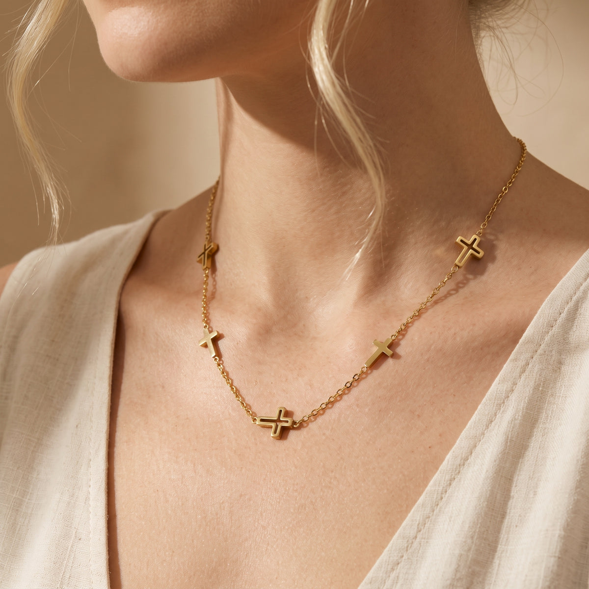 Close-up of a model wearing a gold-tone multi-cross station necklace over a light-colored open-neck garment.
