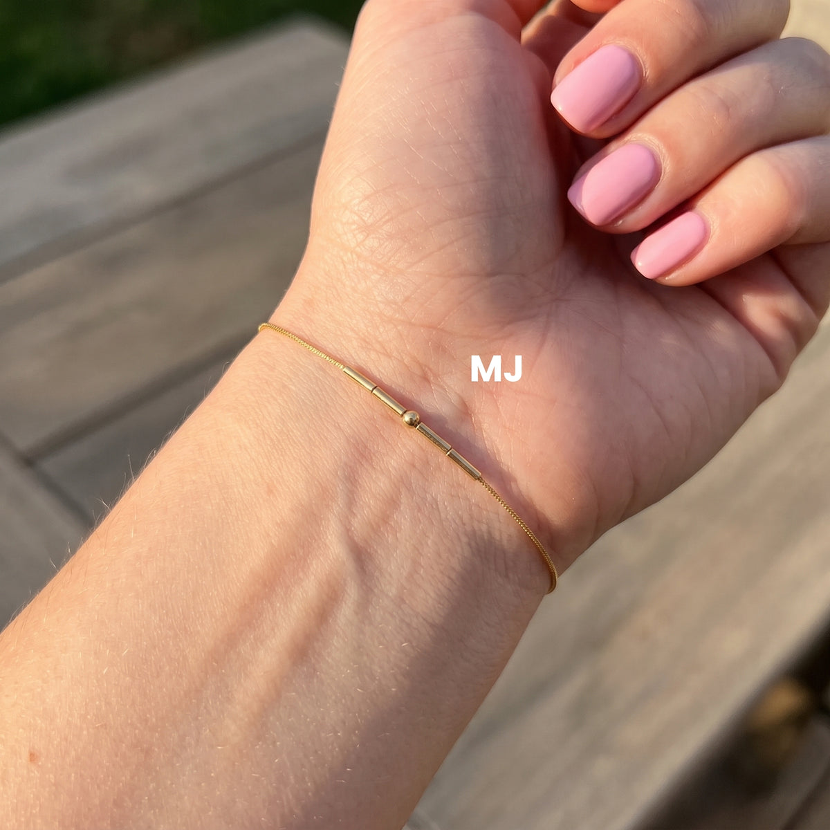 Gold-finish Morse-code bracelet worn on a wrist, with the MJ example label.