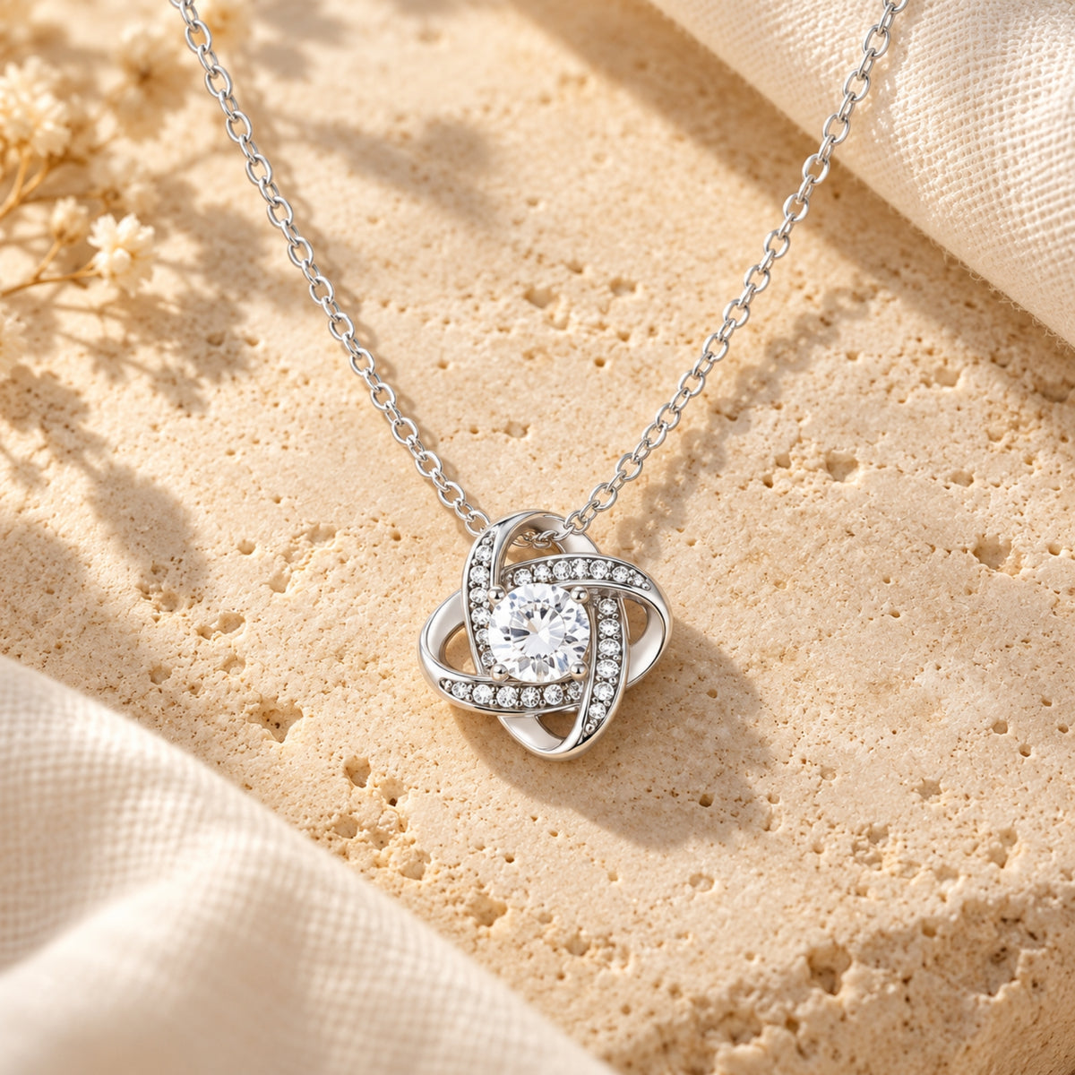 Silver love knot pendant close-up on a pale stone surface.