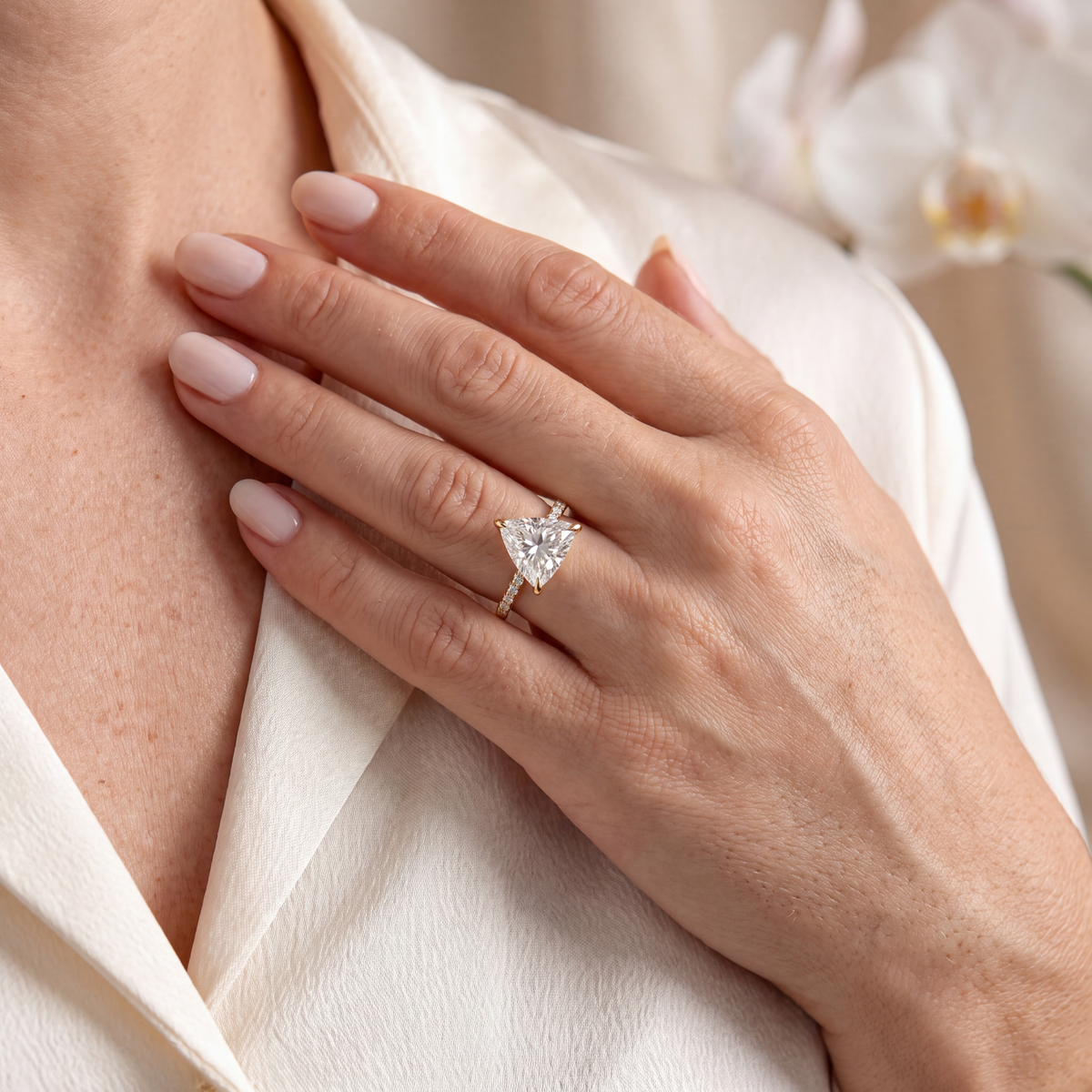 Model wearing a yellow gold trillion-cut moissanite engagement ring with her hand resting on her chest.