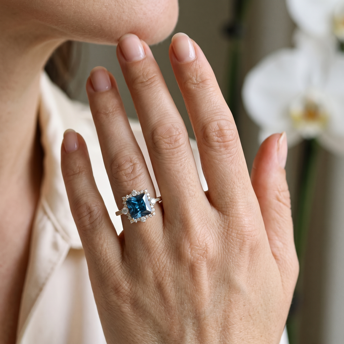 Close-up of a model wearing the rose gold princess-cut blue gemstone halo ring on her finger.