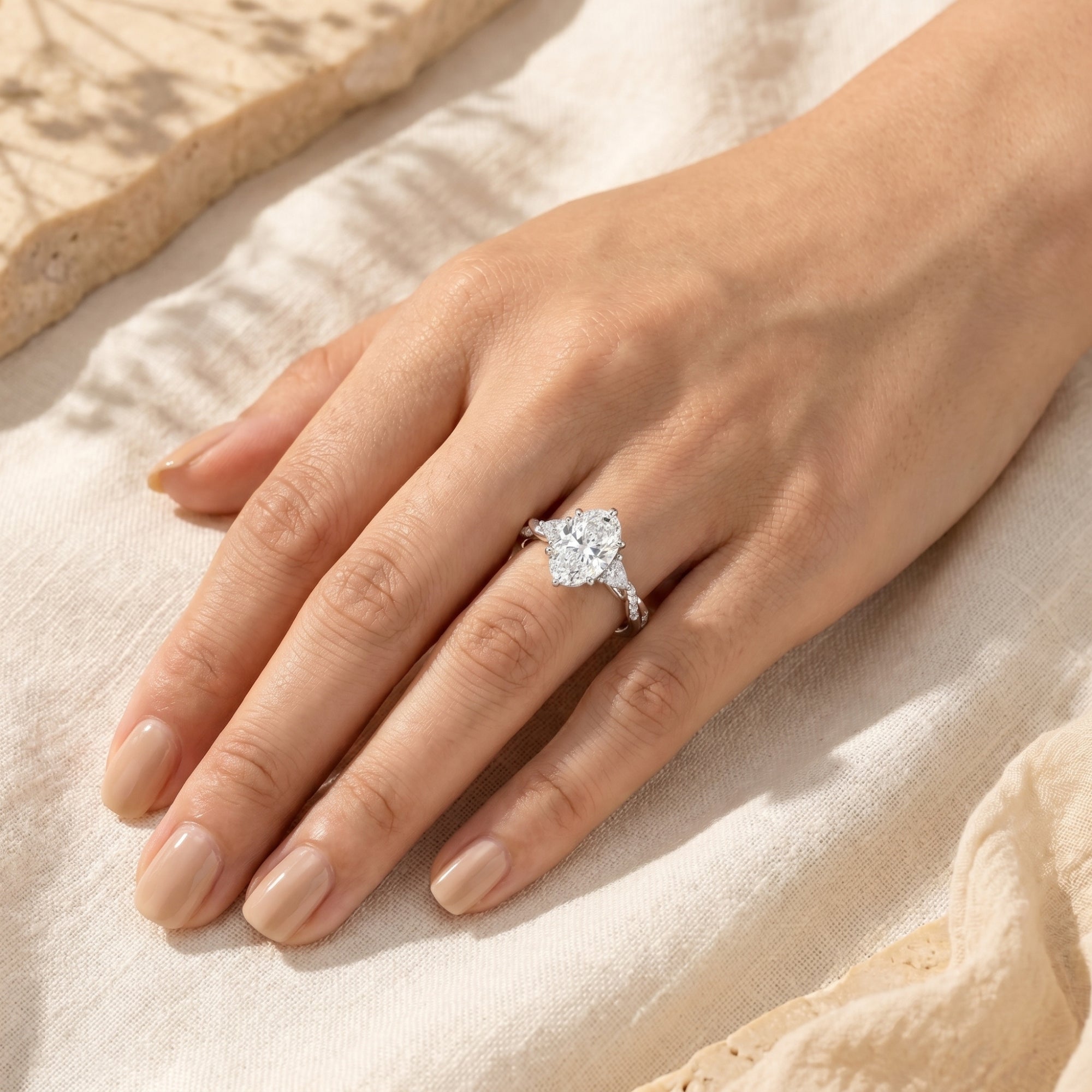Woman wearing the silver Amalthea oval moissanite ring on her hand against a neutral fabric.