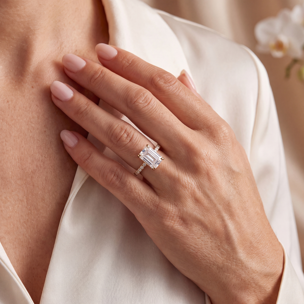 Close-up of a yellow gold emerald cut moissanite engagement ring on a model's hand.