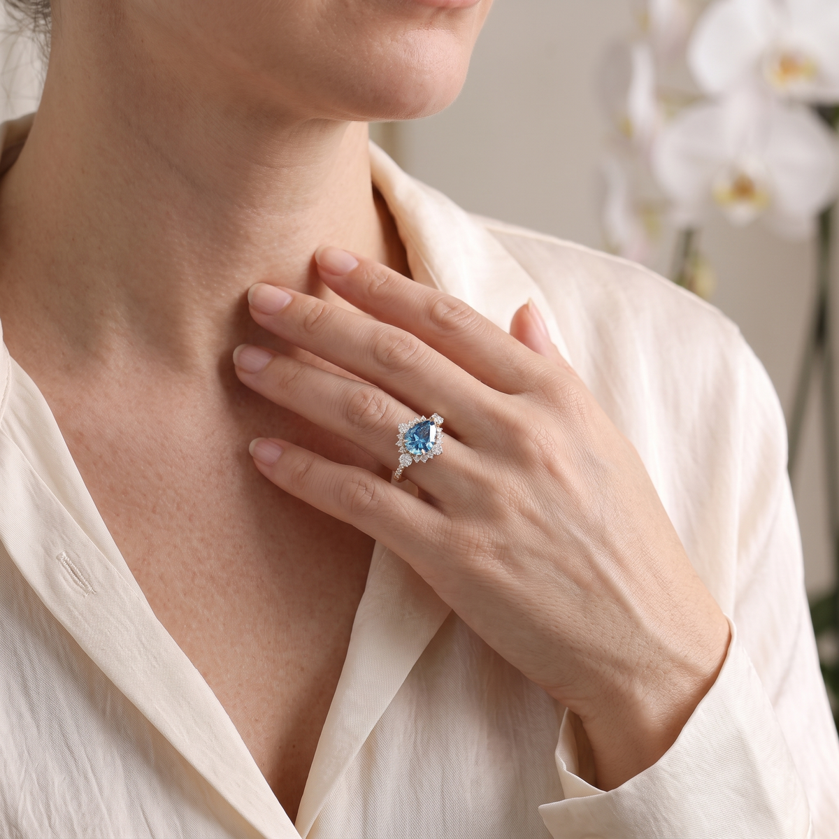 Model wearing the pear cut blue moissanite halo ring in rose gold with white floral accents.