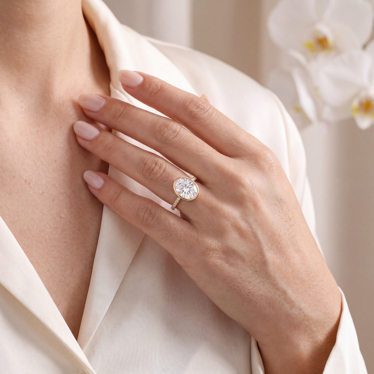 Close-up of a model wearing a gold bezel-set oval moissanite ring.