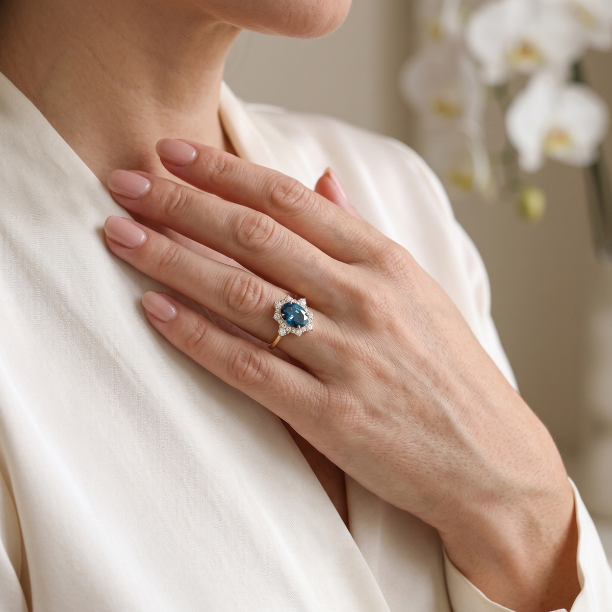 Model wearing a rose gold oval blue moissanite halo ring, resting hand gracefully on chest.