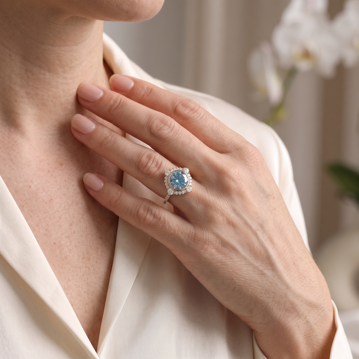 A hand wearing a rose gold halo ring featuring a blue moissanite centerpiece.